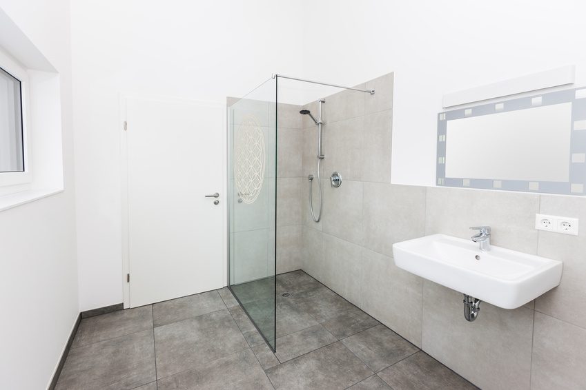 Rahmenlose Walk-In-Glaswand in einem hellen Bad mit grauen Fliesen